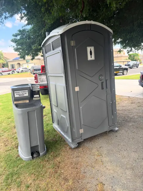 Gray portable toilet with a wash station on a lawn