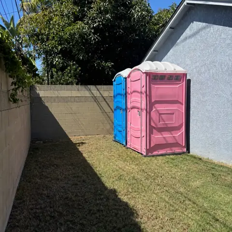 Pink and blue portable toilets set along a backyard fence